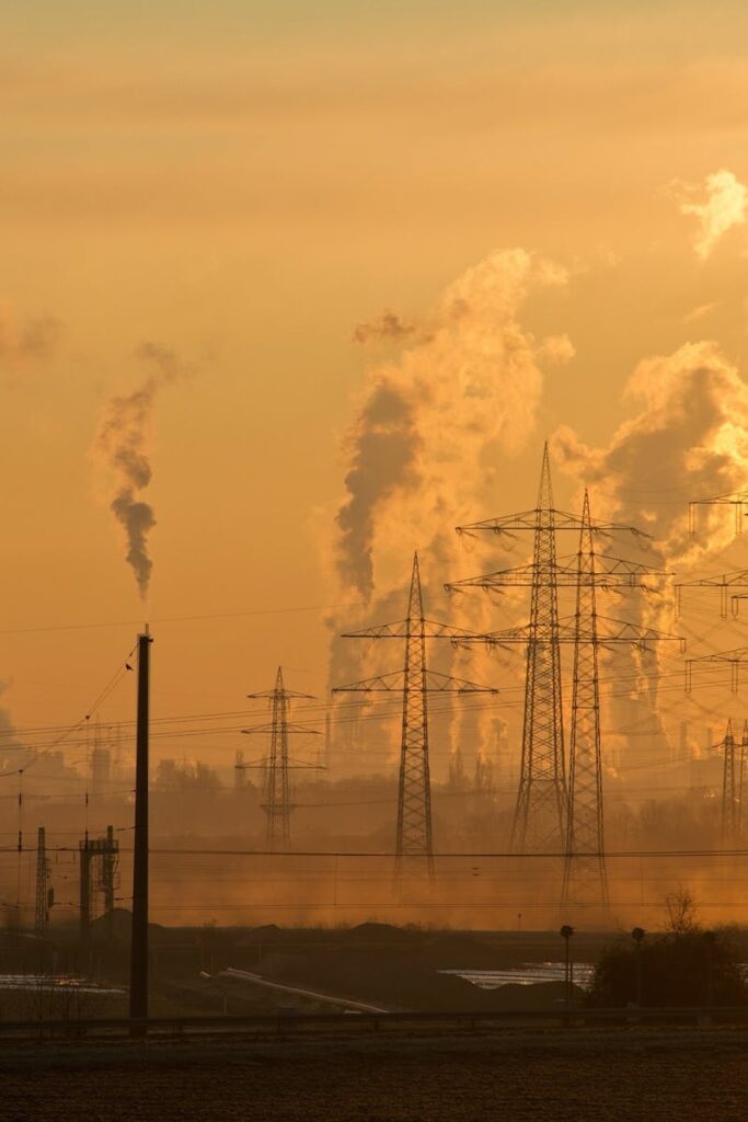 Silhouette of power lines and industrial smoke at sunset, highlighting pollution and energy themes.