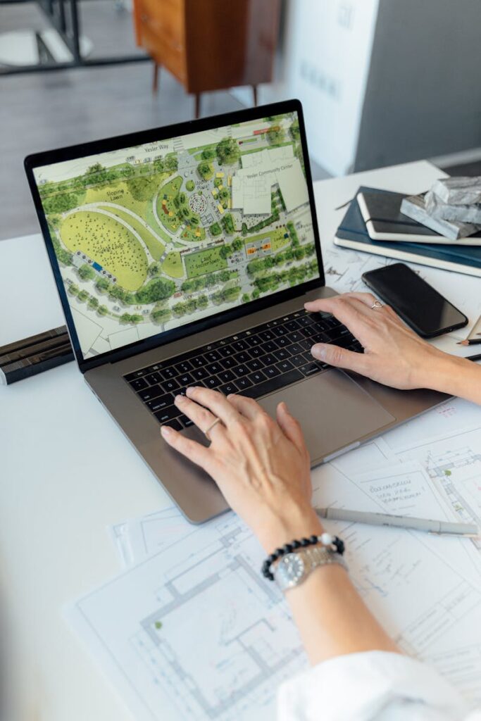 Architect working on landscape plan displayed on laptop with hands typing on keyboard.